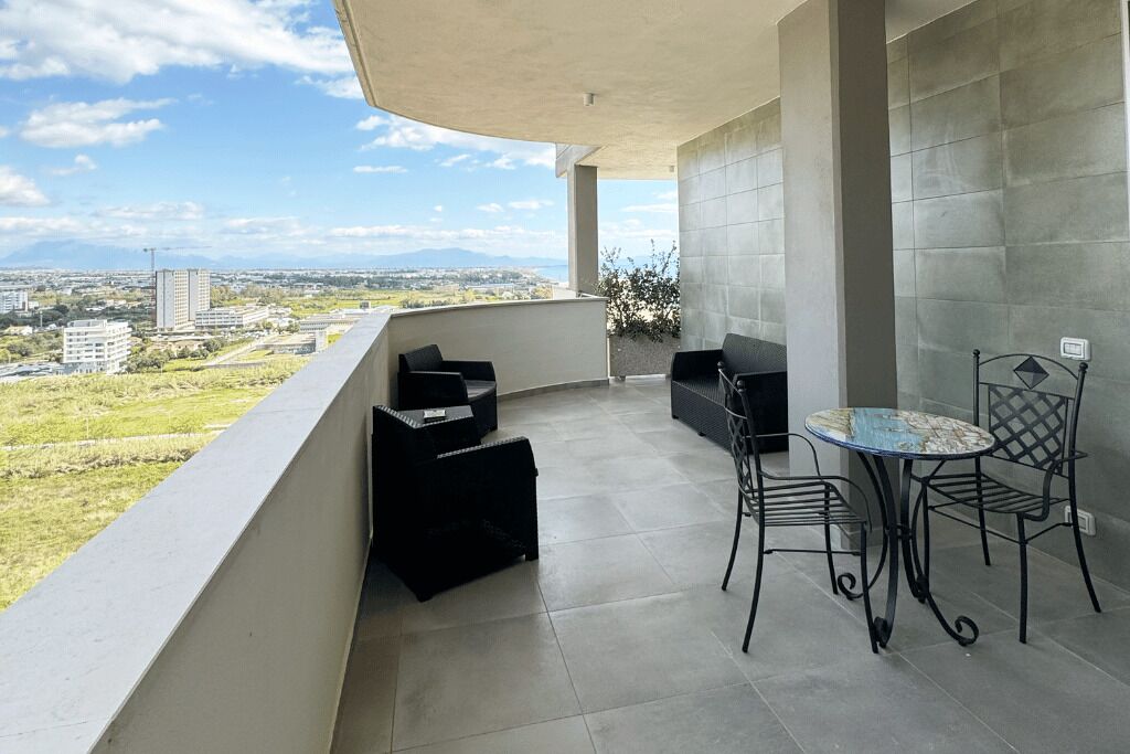 Uma varanda com vista para a cidade, uma mesa redonda com cadeiras e um pequeno sofá preto.