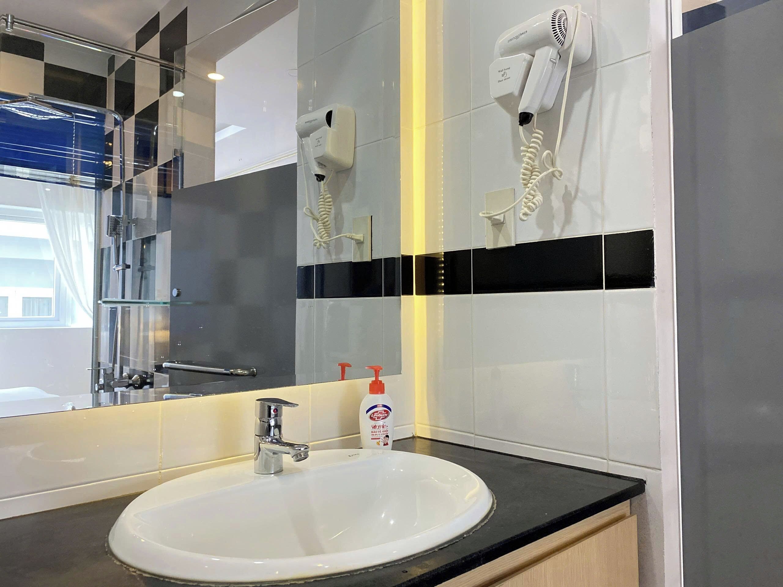 A modern bathroom with a white sink, a handheld hair dryer mounted on the wall, and a glass shower enclosure.