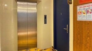 An elevator with a digital display, a blue door, and a fire safety poster on the wall. - MACALLAN HOTEL Phu My Hung- SECC (Ho Chi Minh City)