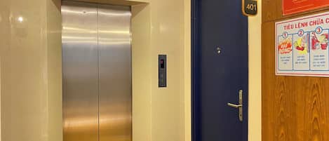 An elevator with a digital display, a blue door, and a fire safety poster on the wall.