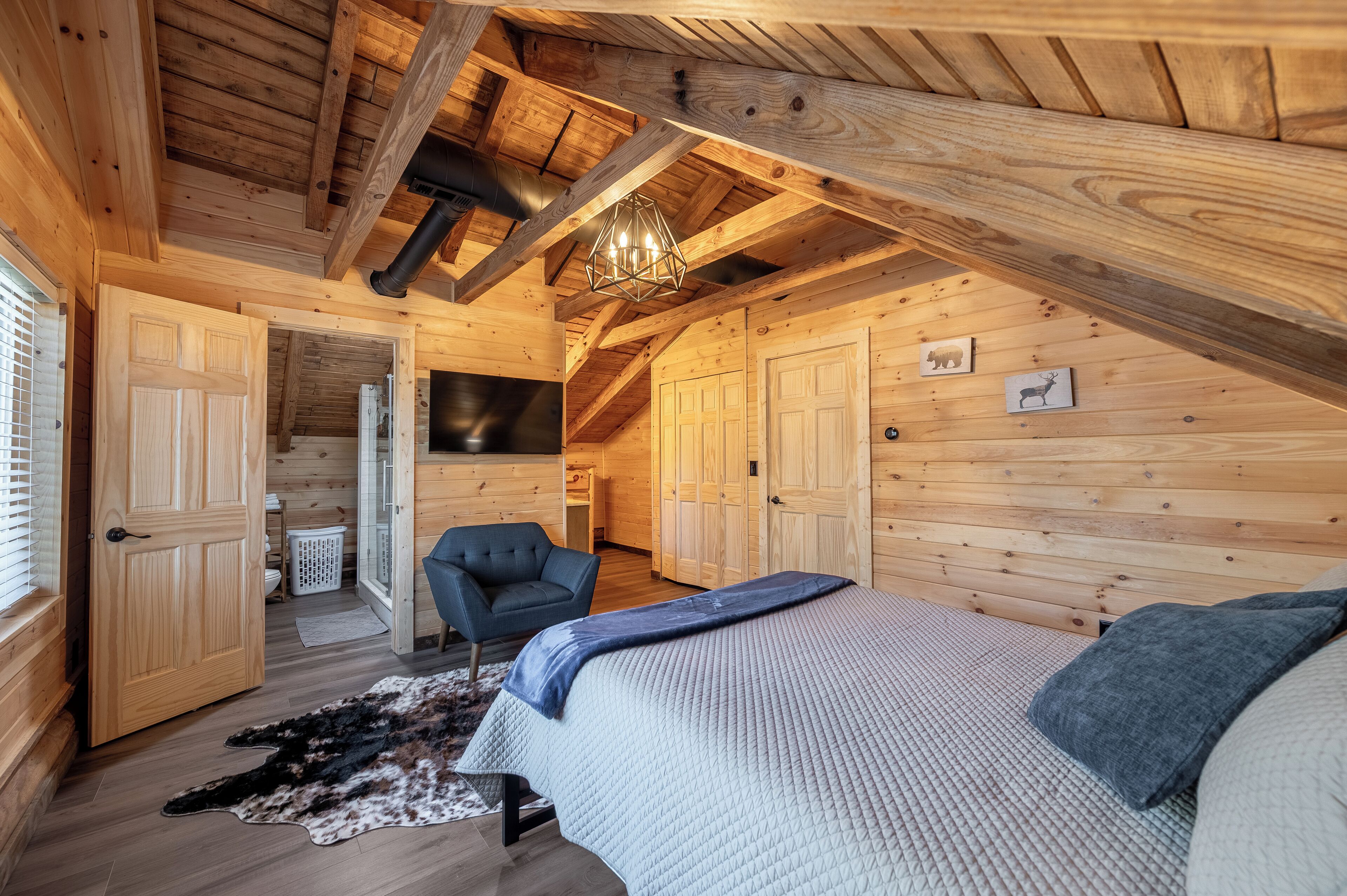 A cozy wooden cabin bedroom with a sloped ceiling, a bed with a quilt, a chair, and a rug.