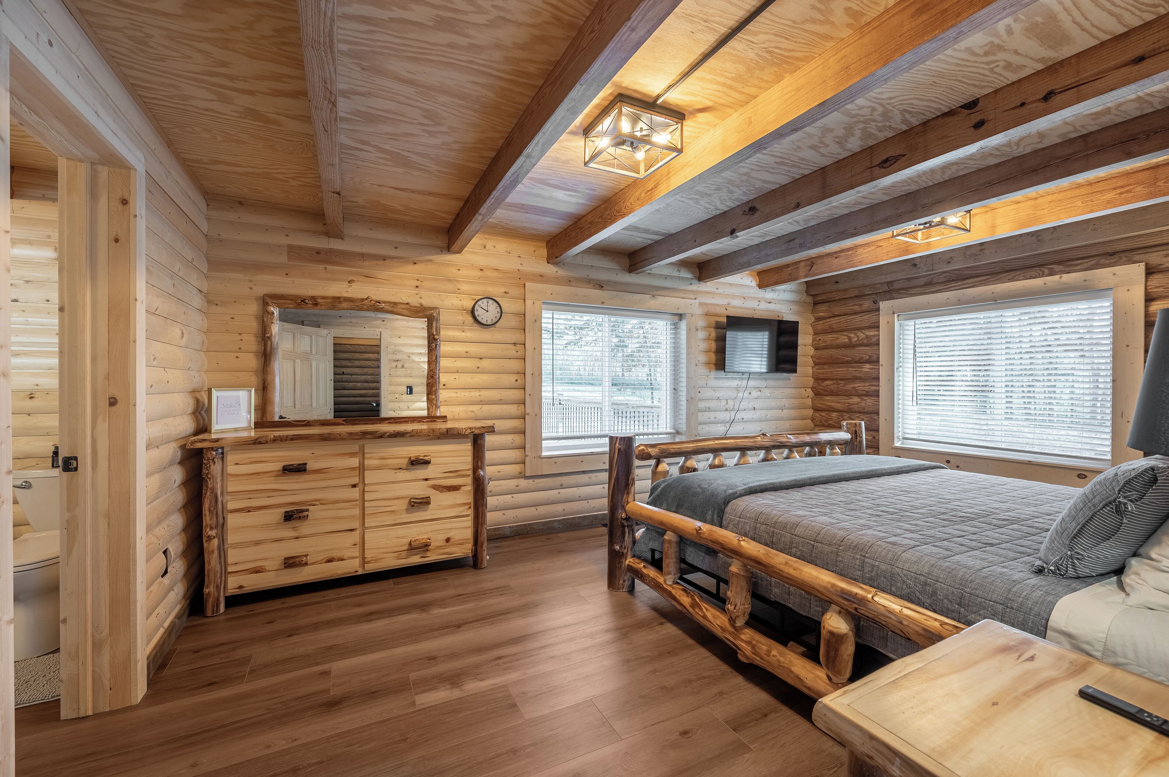 Une chambre située dans une cabane en rondins, avec un lit en bois, une commode et une grande fenêtre.