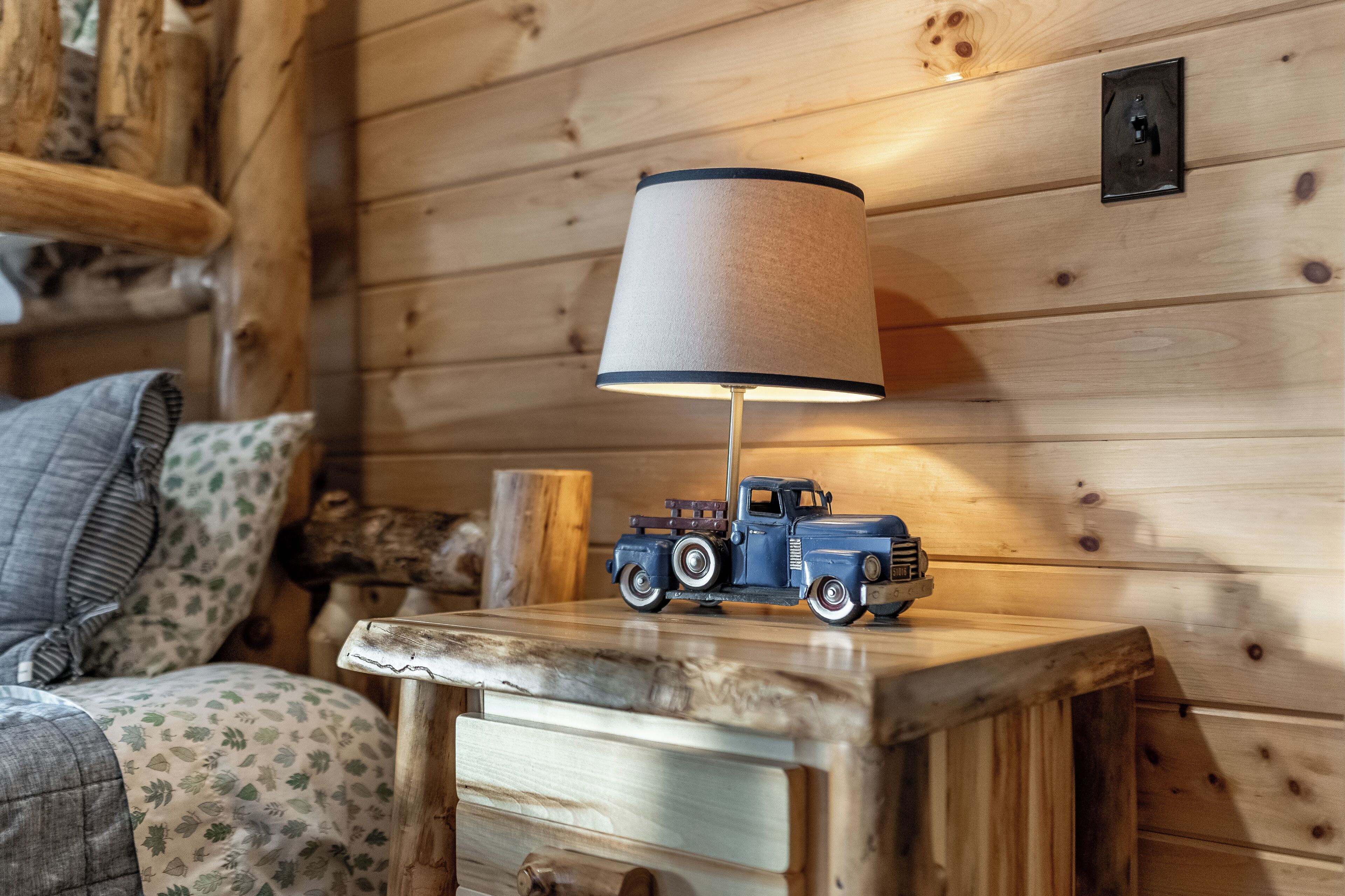 Een houten hutje van binnen, met een tafeltje waarop een speelgoedvrachtwagen en een lamp staan.