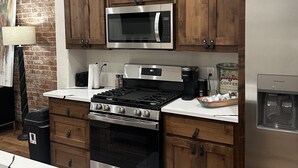 Una cocina con armarios de madera, un microondas de acero inoxidable, una estufa a gas y un refrigerador.