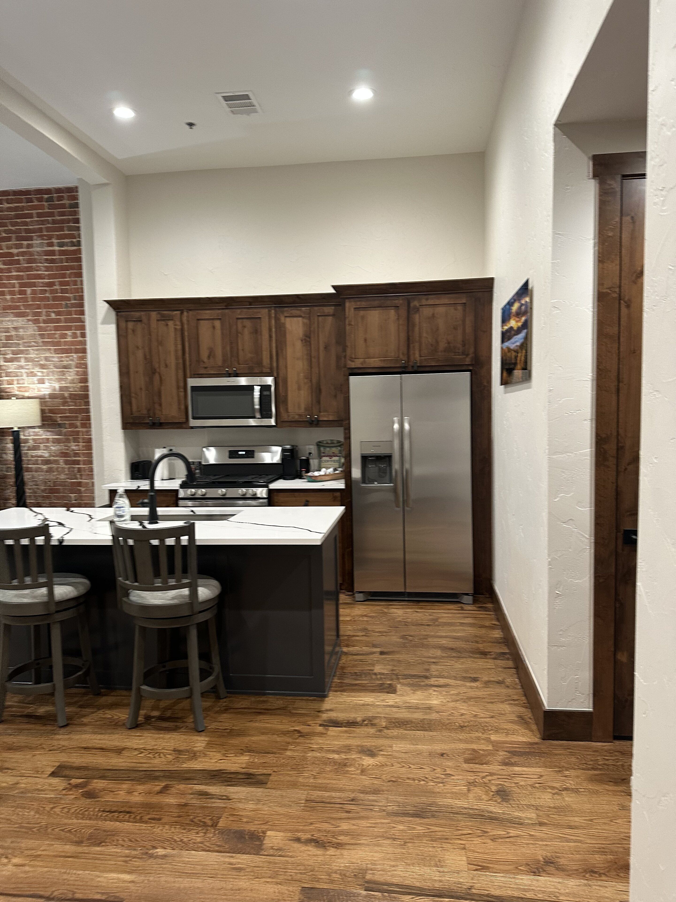 A compact kitchen with wooden cabinets, a stainless steel refrigerator, a microwave, and a sink.