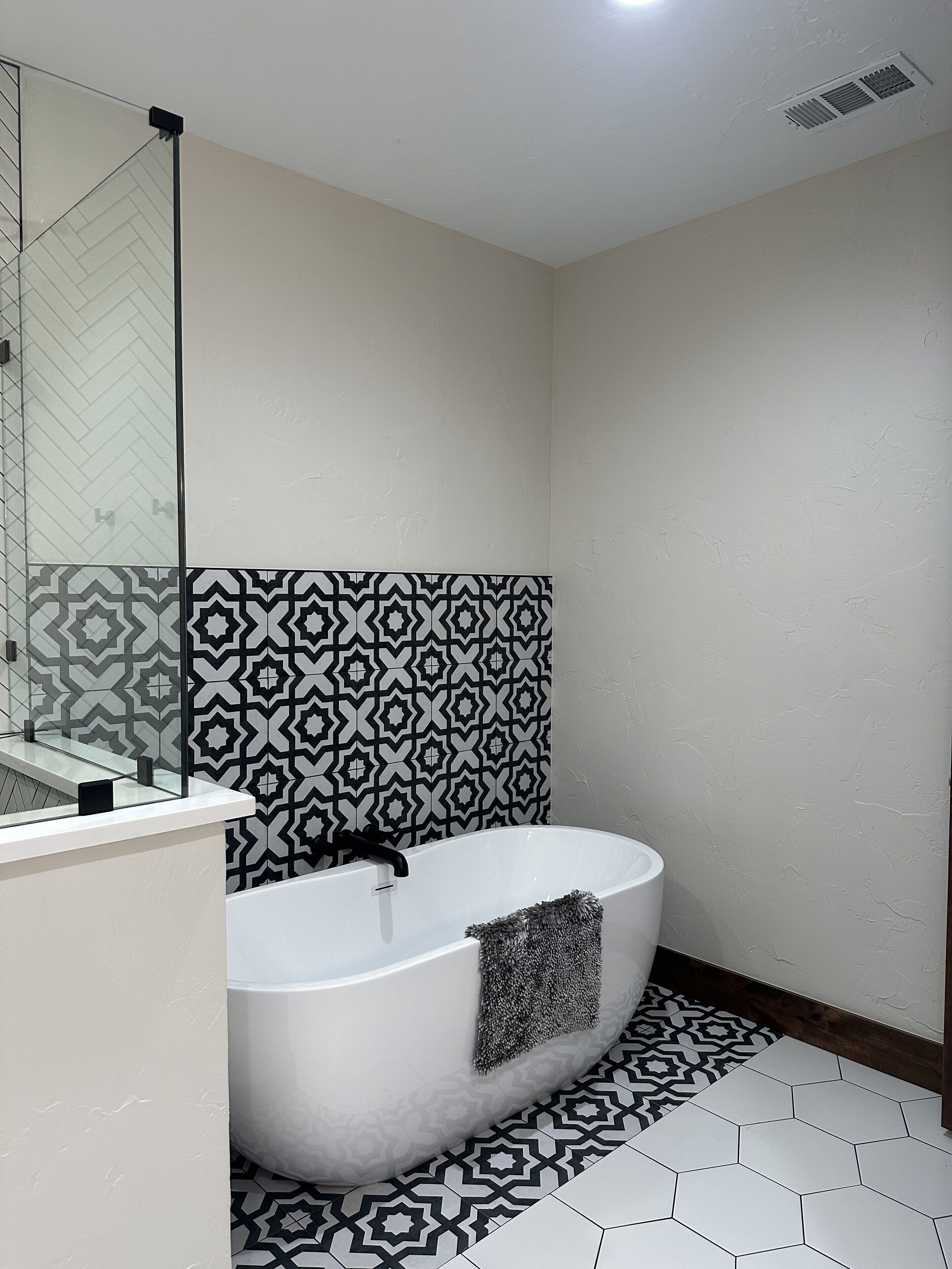 Un baño moderno con una bañera independiente, azulejos estampados y un cerramiento de ducha de vidrio.