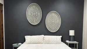 Un dormitorio con una cama grande, dos platos decorativos colgados en la pared, un ventilador de techo y una mesita de noche con lámpara.