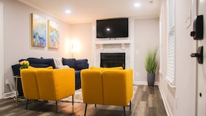 A living room with a fireplace, a flat-screen TV, and two yellow armchairs. - Fayetteville Elite Escape – Close to Base & VA Hospitals (Fayetteville)