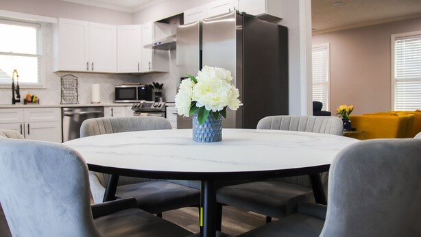 A modern kitchen with white cabinets, stainless steel appliances, and a round dining table with grey upholstered chairs. - Fayetteville Elite Escape – Close to Base & VA Hospitals (Fayetteville)