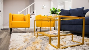 A modern living room with a yellow sofa, a blue sofa, and a glass coffee table. - Fayetteville Elite Escape – Close to Base & VA Hospitals (Fayetteville)