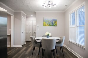 A dining area with a round table, four chairs, and a vase of flowers. - Fayetteville Elite Escape – Close to Base & VA Hospitals (Fayetteville)
