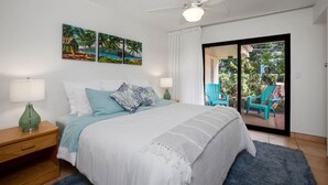 A bedroom with a bed, two nightstands, a ceiling fan, and a view of an outdoor patio with chairs. - Zen by the Sea Ground-level Paradise With Ocean Views Whales Watching (Lahaina)