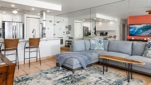 A modern kitchen with white cabinets, a large island, and a dining area with wicker chairs. - Zen by the Sea Ground-level Paradise With Ocean Views Whales Watching (Lahaina)