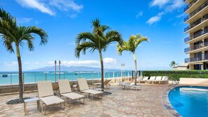 A poolside area with lounge chairs and palm trees, overlooking a clear blue ocean and a mountain in the distance. - Zen by the Sea Ground-level Paradise With Ocean Views Whales Watching (Lahaina)
