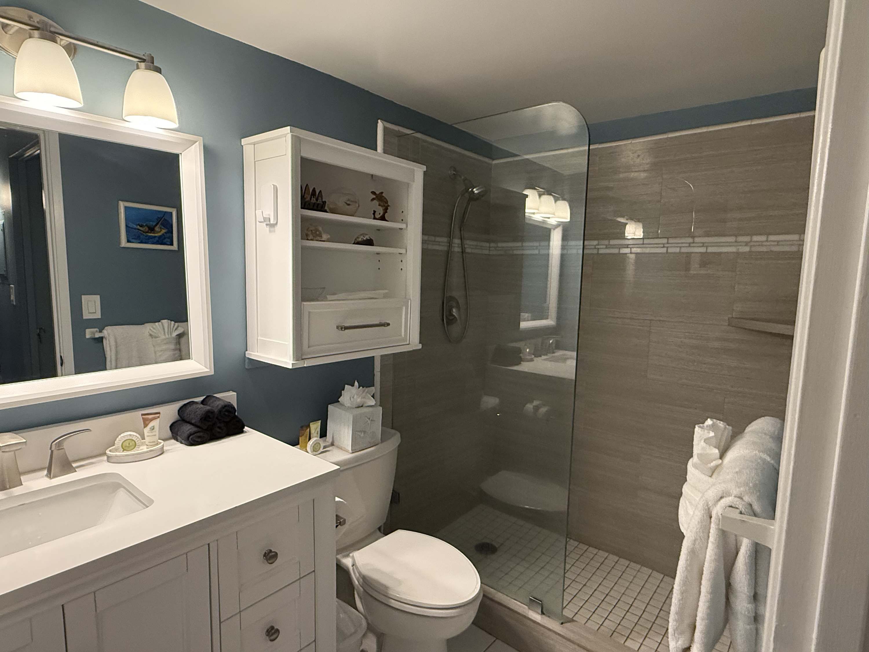 A modern bathroom with a white vanity, a large mirror, a glass-enclosed shower, and a blue accent wall.