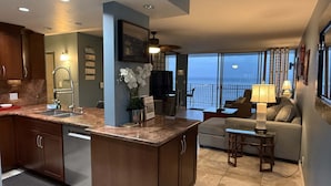 A modern kitchen with a large island, a dining area with a view of the ocean, and a cozy seating area with a balcony overlooking the sea. - Whale Watching Oceanfront Escape Molokai Views Cool Tropical Breezes (Lahaina)