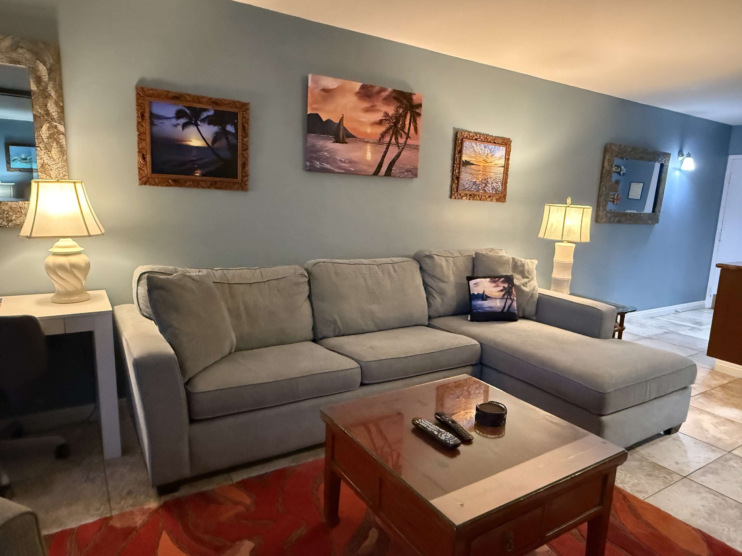 A living room with a grey sofa, a coffee table, and three framed paintings on the wall.