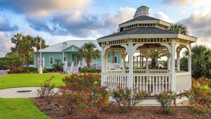 A gazebo with a white picket fence, surrounded by a garden with red flowers and palm trees.