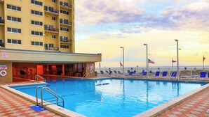 A swimming pool with a checkered floor, lounge chairs, and a building with balconies.
