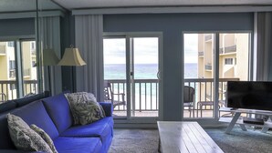 A room with a blue sofa, a TV on a stand, and a view of the ocean through large sliding doors.