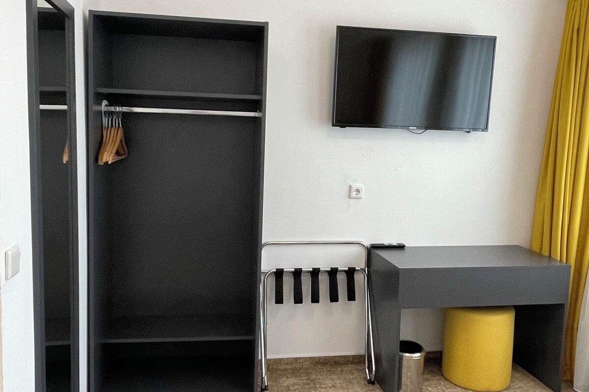 A hotel room with a wardrobe, a desk, a television, and a yellow accent wall.