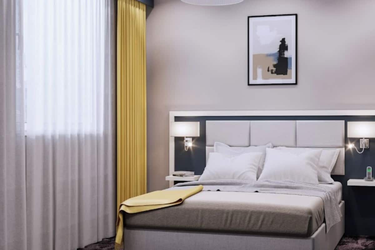 A modern hotel room with a large bed, bedside tables, a nightstand, a lamp, and a framed picture on the wall.