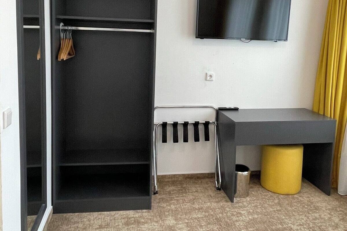 A hotel room with a wardrobe, a desk, a television, and a yellow accent wall.
