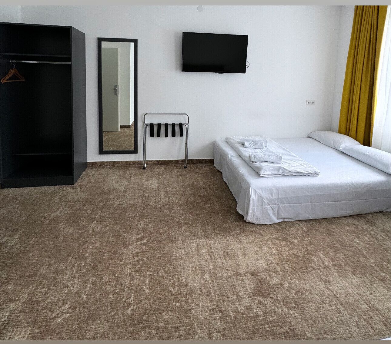 Una habitación de hotel con cama, armario, espejo, televisor y radiador.
