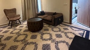 A living room with a sofa, armchair, ottoman, and a patterned rug. - Hôtel La Pivoine (Abidjan)