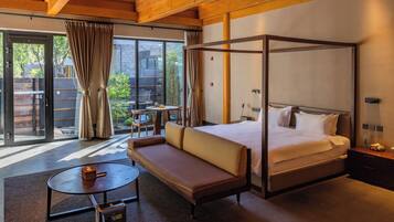 Habitación de hotel moderna con cama con dosel, un sofá, una pequeña mesa redonda y vistas al exterior a través de amplias ventanas.