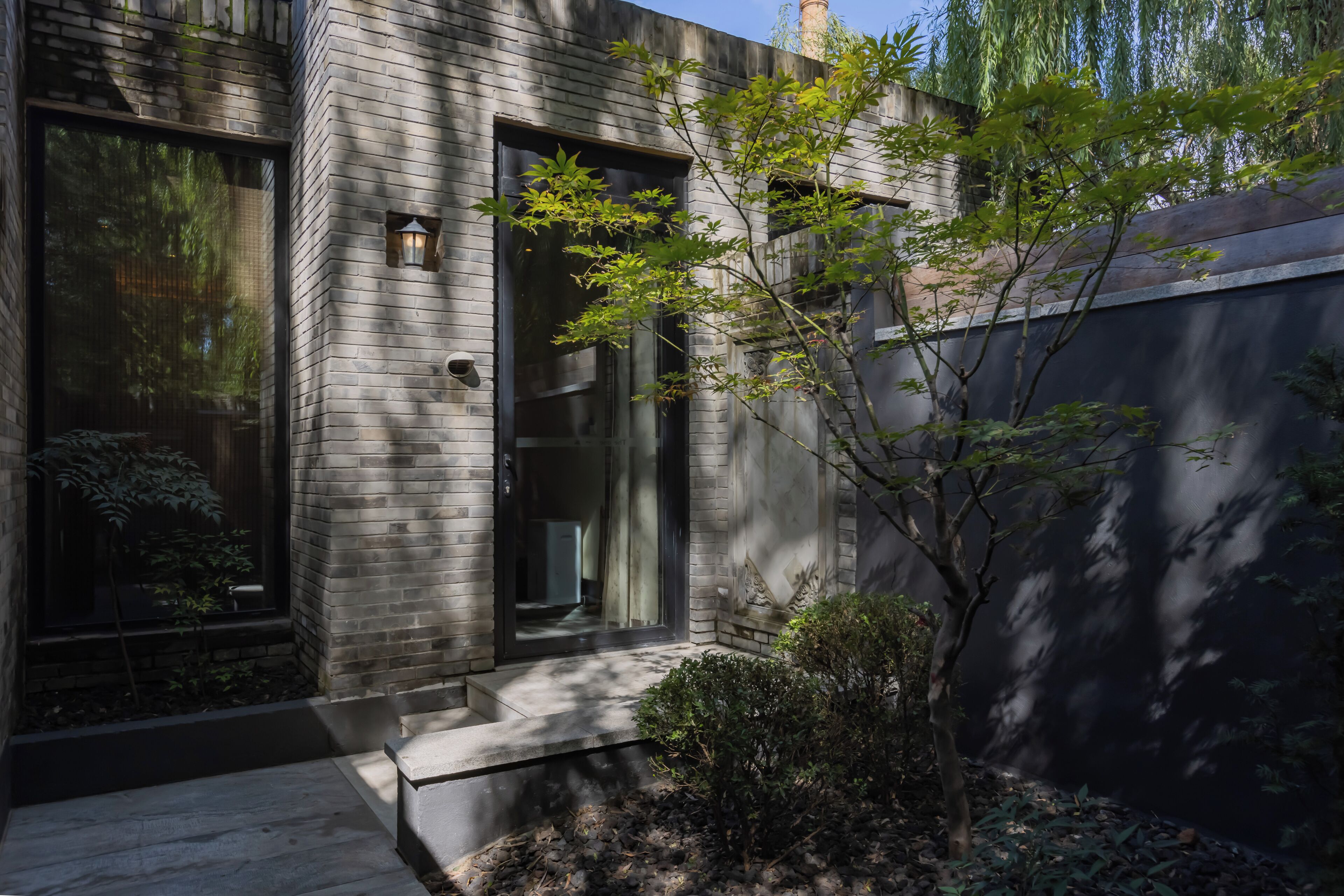 A modern building with a brick facade, large windows, and a small tree in the foreground.