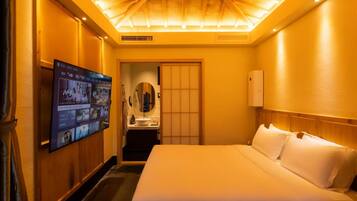 A hotel room with a large bed, a television mounted on the wall, a bathroom with a sink and mirror, and a ceiling with recessed lighting.