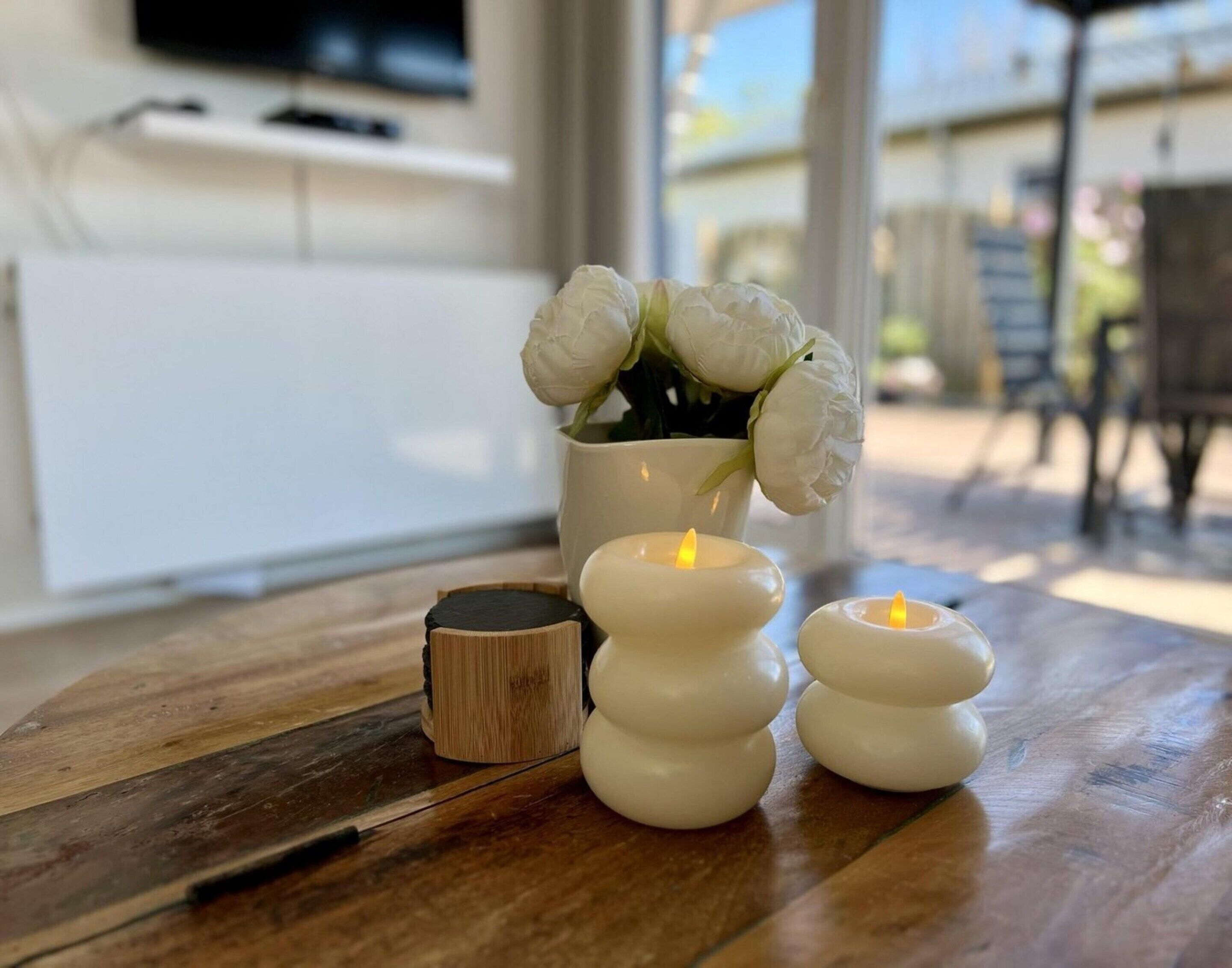 Une table en bois sur laquelle se trouvent un chandelier blanc, une bougie et une plante en pot ornée de fleurs blanches.