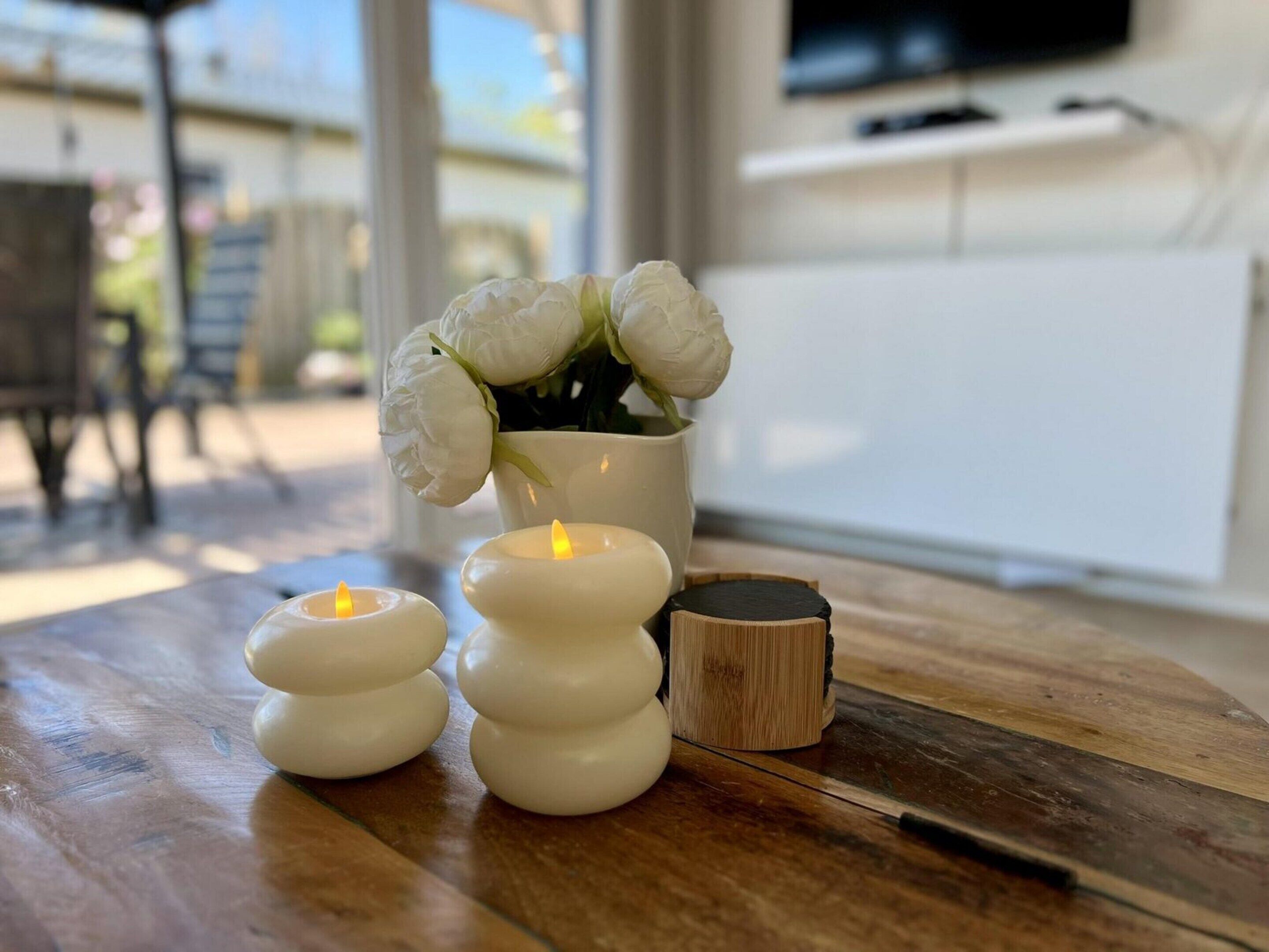 A wooden table with three white candles and a vase with white flowers.