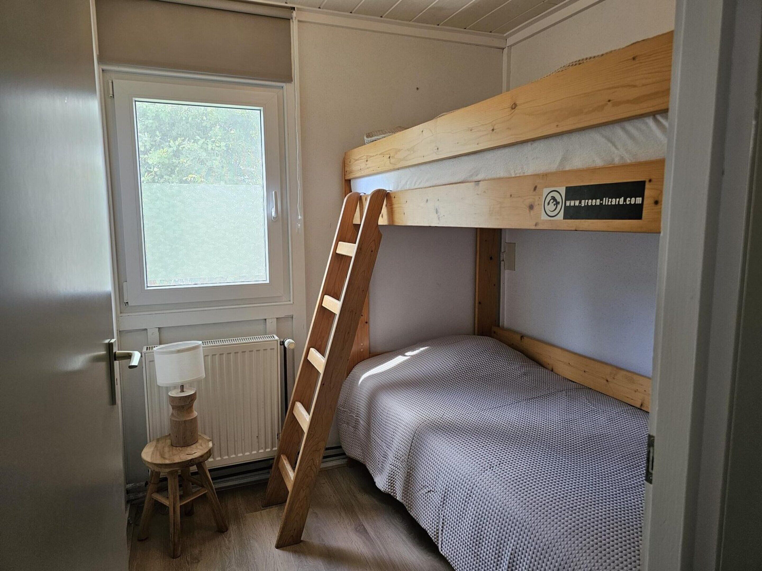 Une chambre avec un lit superposé, une petite échelle, un petit tabouret et une fenêtre.