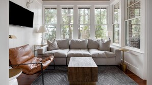A modern living room with a sectional sofa, a leather armchair, a wooden coffee table, and a TV mounted on the wall. - Luxe interiors, pet-friendly & fireplace on the porch (Bluffton)