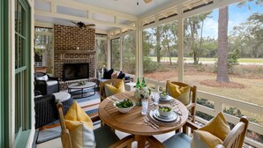 A covered patio with a brick fireplace, outdoor furniture, and a view of the surrounding landscape. - Luxe interiors, pet-friendly & fireplace on the porch (Bluffton)