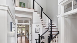A spacious hallway with a wooden floor, a black and white staircase, and a chandelier. - Luxe interiors, pet-friendly & fireplace on the porch (Bluffton)