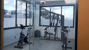Une salle de sport moderne avec des murs en verre, divers appareils d’exercice et une vue dégagée sur le ciel.