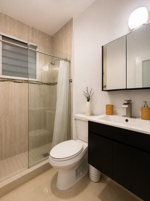Une salle de bain moderne avec une douche à parois de verre, des toilettes blanches, un meuble-lavabo avec un miroir et un évier.