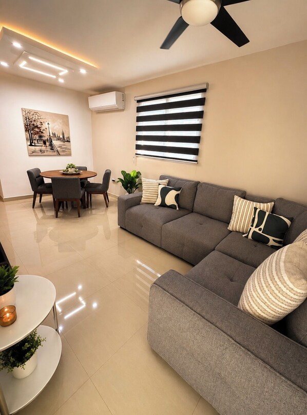 Un salon moderne avec un canapé gris, une table de salle à manger ronde et un ventilateur de plafond.