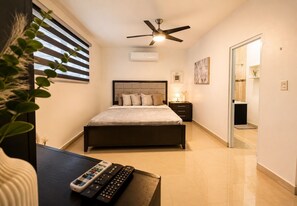 Une chambre à coucher comprenant un lit, une table de chevet, une commode, un ventilateur de plafond et un téléviseur.