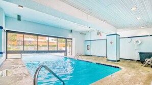 Una piscina interior amb aigua cristal·lina, una escala metàl·lica i vista a edificis exteriors.