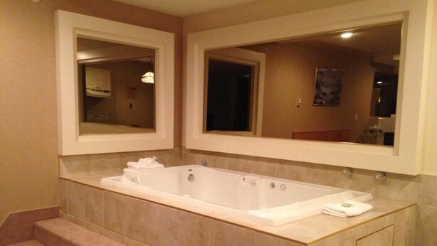 A bathroom with a large bathtub, two mirrors, and a trash can.