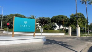 Señal de Balalia Golf Village con una señal de alto y palmeras al fondo.