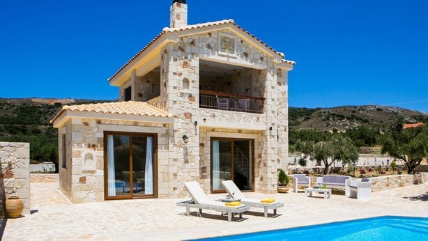 Une maison en pierre à deux étages, dotée d’une piscine et d’un espace de détente extérieur.