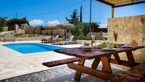 Un espace aménagé au bord de la piscine, avec une piscine en pierre, des chaises longues en bois, une table de pique-nique et un mur en pierre.