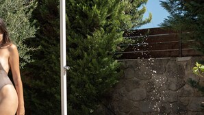 Une fontaine en pierre dotée d’un pommeau de douche, entourée de verdure et bordée d’un mur de pierre.
