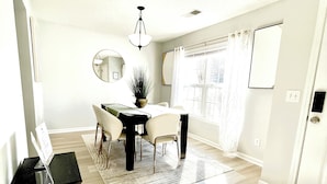 A modern dining area with a round table, chairs, a potted plant, and a black side table with a menu stand.