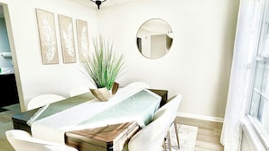 A dining area with a table, chairs, a plant, and a mirror on the wall.